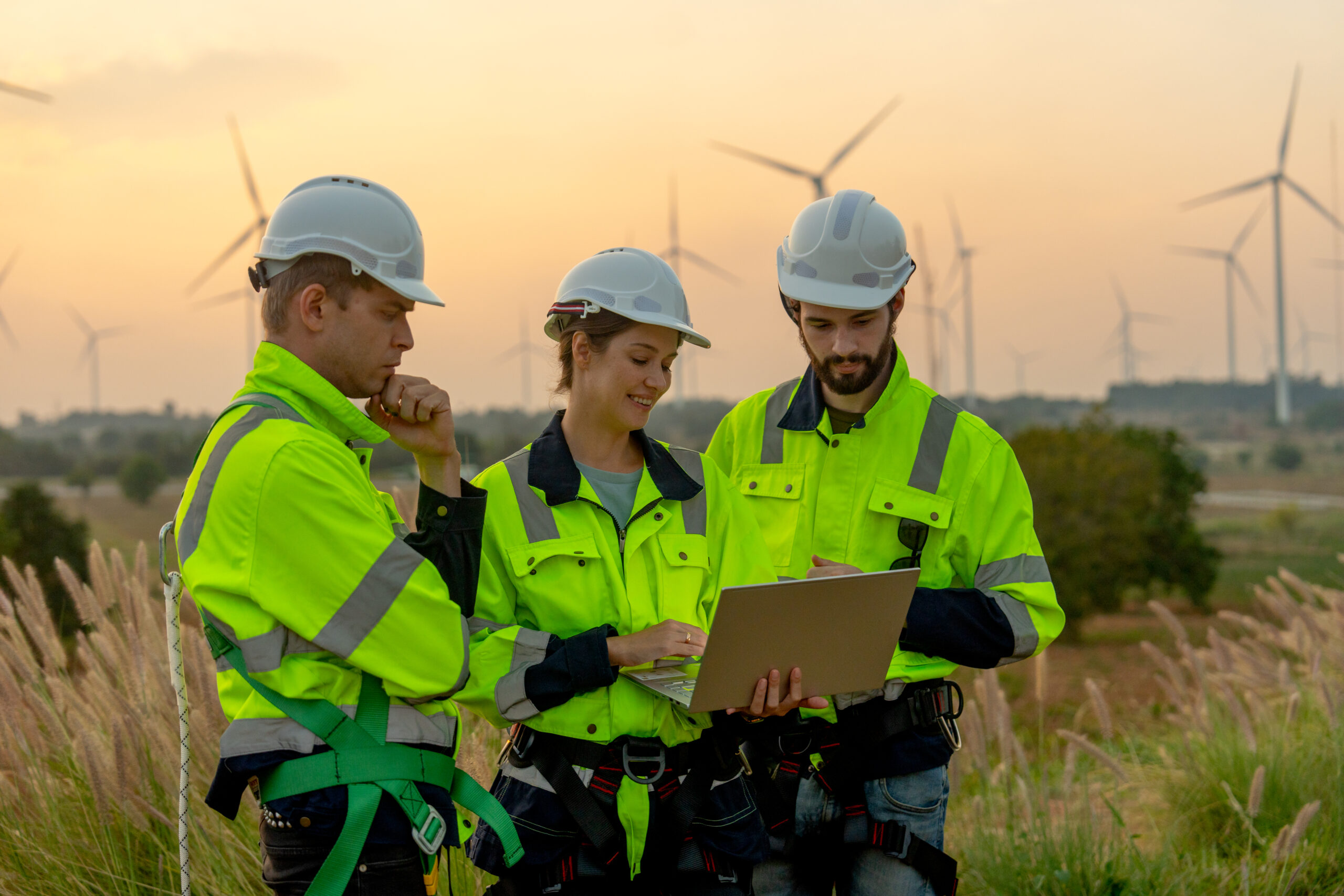 Close up group of technician workers man and woman work using laptop and stay in front of windmill or wind turbine